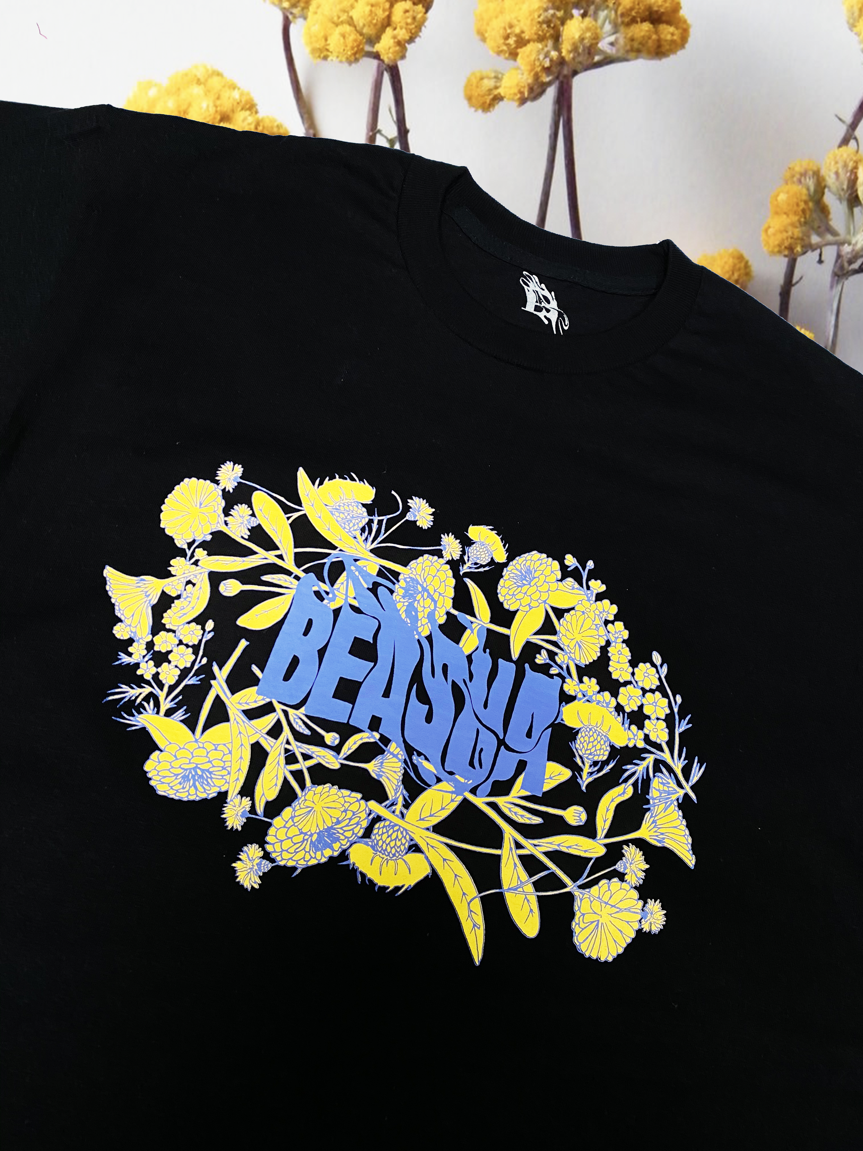 black T-shirt with yellow and lilac floral screen print in boxy silhouette with round neck.